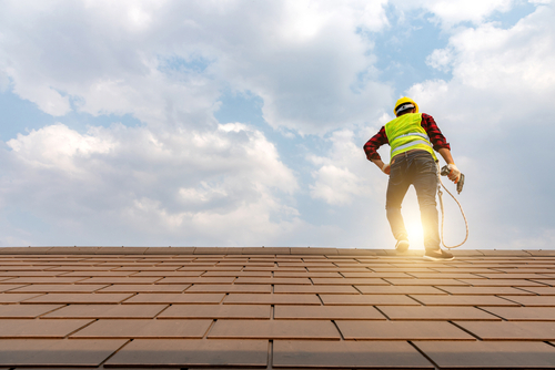 commercial roofer stands on roof while sun shines before him