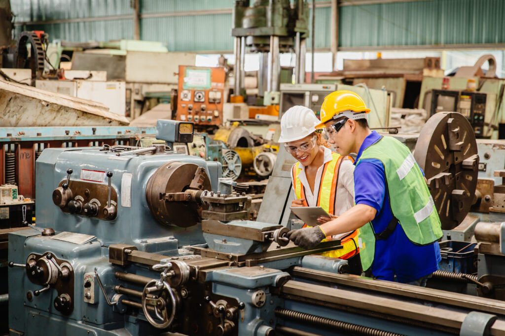 Two workers in a manufacturing facility smiling and doing their jobs.