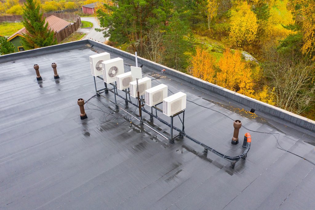A commercial roof with scattered ventilation pipes surrounding a row of small, raised HVAC boxes