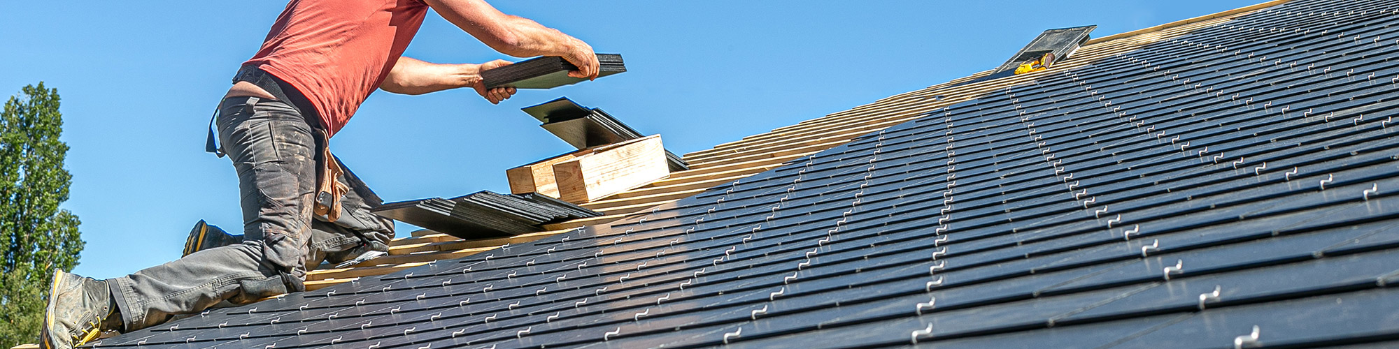 A worker installs slate roofing tiles on a home.