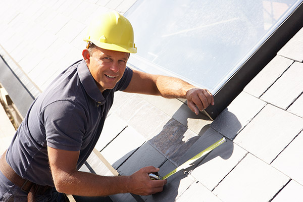 A man in a hard hat works on a slate roof.