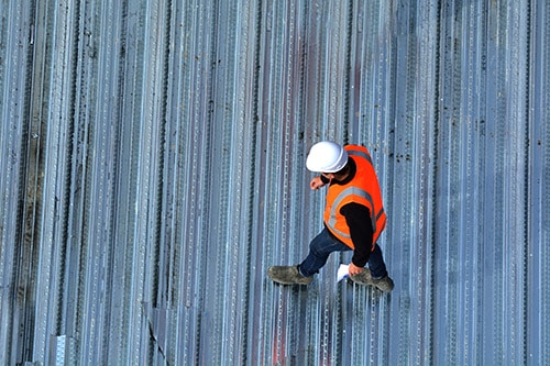 A roofing inspector walks on a metal roof.