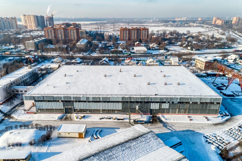 A large commercial warehouse with snow on the roof and surrounding areas.