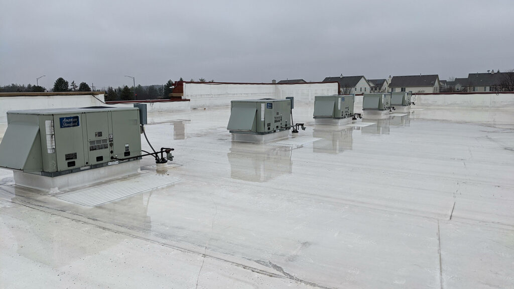 A row of HVAC boxes installed on a commercial roof covered by a sheen of water.