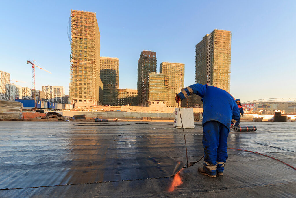 A roofing contractor uses a flame to melt sealant on a built-up roof