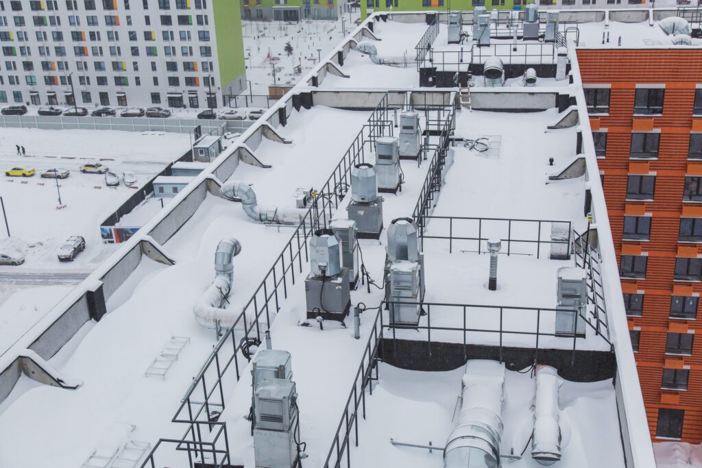 A bird's-eye view of a commercial roof with a robust HVAC and ducting system, as well as a central platform. The entire scene is covered in snow.