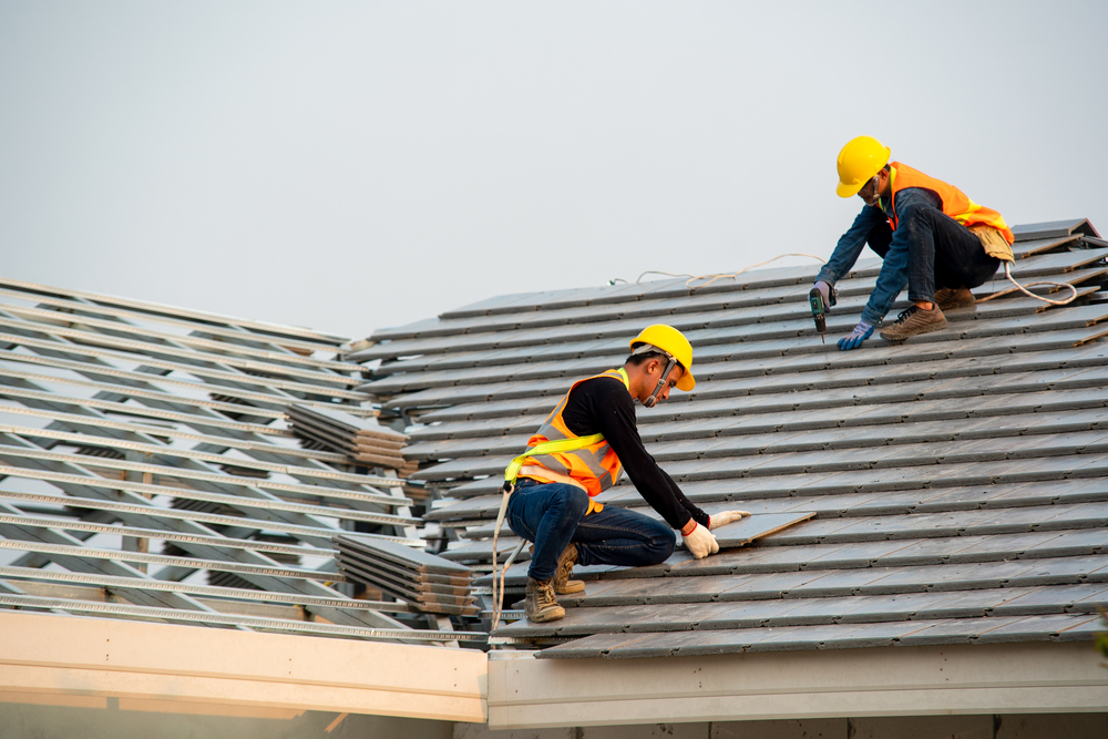 Two roofers installing concrete roof tile on a building.